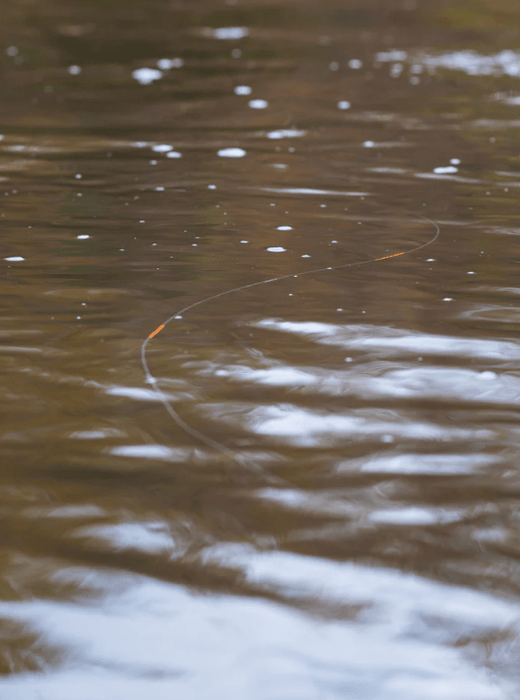 A close-up view of a fishing line cast across rippling brown water, with small white bubbles and reflections on the surface.