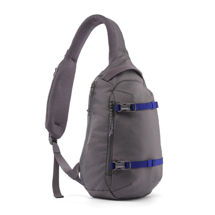 A gray sling backpack with two blue compression straps and silver buckles, shown from a side profile view on a white background.