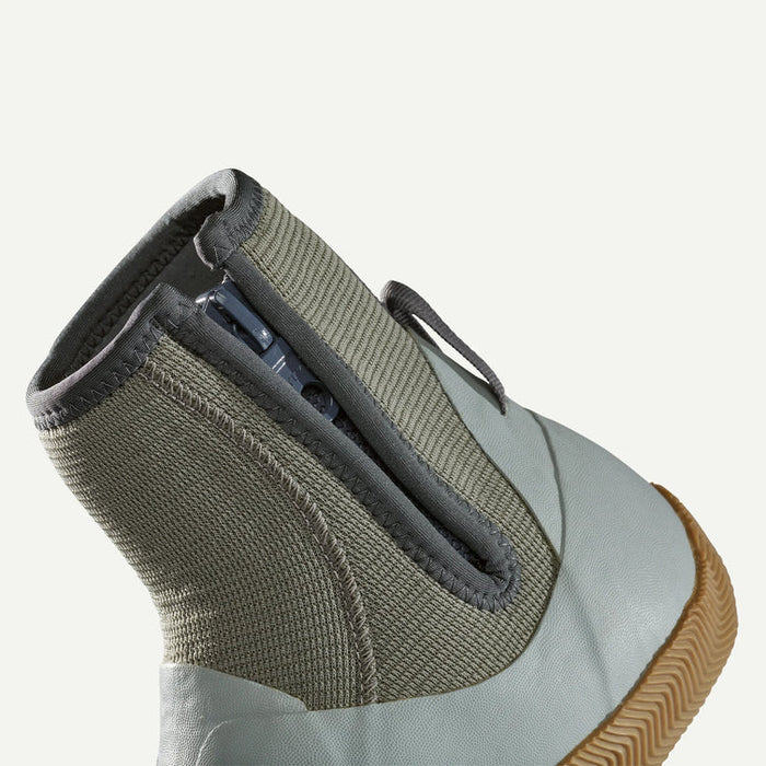 Close-up of the side and heel of a mid-calf slip-on shoe with a textured olive green knit collar, a light gray synthetic upper, and a brown gum sole, shown against a plain off-white background.