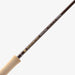 A close-up of a Redington Classic Spy fly fishing rod blank, showing the dark brown graphite shaft with gold and white branding text, and the natural cork handle on a light gray background.