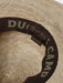 Interior view of the Duck Camp Crushable Flats Hat, highlighting the comfortable dark brown moisture-wicking sweatband printed with the repeating "DUCK CAMP" brand name and a "100% STRAW" fabric tag.