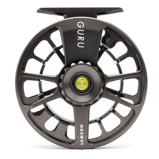 A close-up studio shot of a fly fishing reel spool, featuring a dark metallic gray body with cutout spokes, the brand name 'GURU' printed vertically on the top arm, and 'LAMSON' on the lower arm, with a small yellow-green center button.