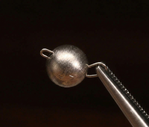 Size 1 Hareline Insta Jig 2.0 tungsten weights in Nickel, showcasing the 0.6-gram keeled bodies coated in a high-visibility, smooth nickel finish held on a vice.