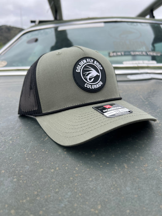 Green w/ Rope variant of the Golden Fly Shop 112 Trucker Hat 2026 showcasing a sage green crown, black mesh back, thin black accent rope, and circular rubber fly logo patch