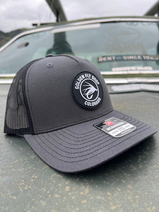 Grey variant of the Golden Fly Shop 112 Trucker Hat 2026 displaying a solid dark grey structured front crown, matching grey mesh backing, and circular rubber fly logo patch