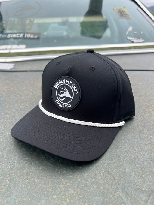 Front angled view of the Golden Fly Shop Hat 258 in solid black featuring a thick white accent rope and a circular black rubber fly silhouette logo patch
