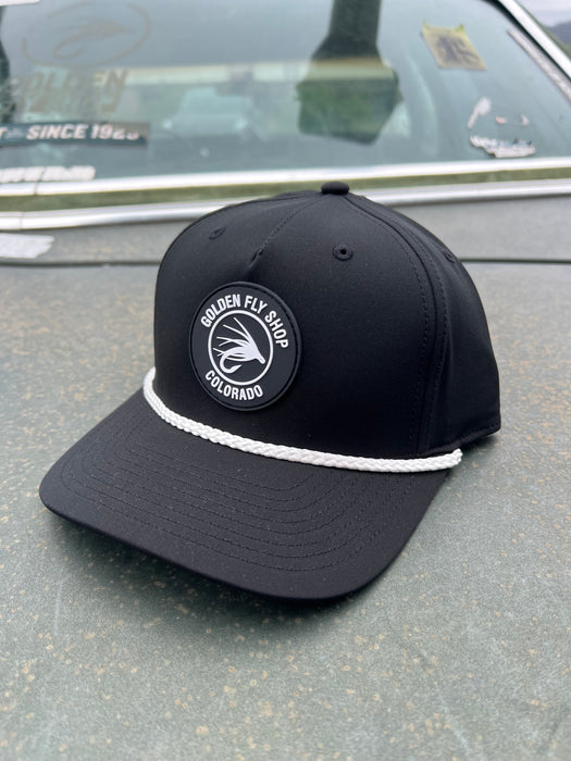 Front angled view of the Golden Fly Shop Hat 258 in solid black featuring a thick white accent rope and a circular black rubber fly silhouette logo patch