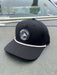 Front angled view of the Golden Fly Shop Hat 258 in solid black featuring a thick white accent rope and a circular black rubber fly silhouette logo patch