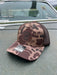 Front profile view of the Golden Fly Shop Hat 112 Bark Duck Camo resting on a car hood showcasing the structured camouflage crown and circular stitched leather fly logo patch