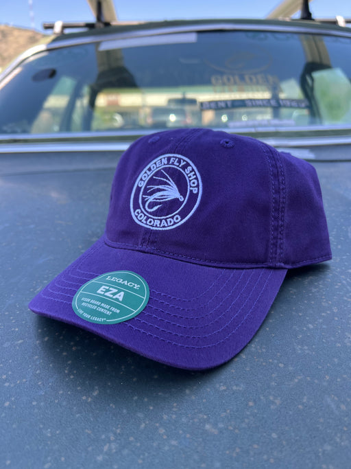 Purple variant of the Golden Fly Shop Dad Hat 2026 resting on a car hood showcasing the unstructured cotton crown and circular embroidered fly logo patch