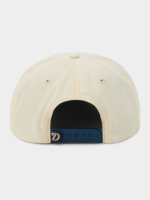 Back view of a cream-colored snapback cap with a dark blue adjustable strap and a small silver metal D-ring closure, shown on a light gray background.