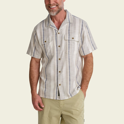 Front view of a man wearing the Howler Brothers Shores Club Shirt in Old Bill Stripe Limestone featuring a camp collar and khaki shorts