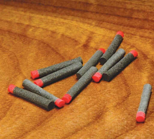 A collection of Hareline 1/16 inch High Viz Ant Bodies scattered on a wooden bench, showcasing the segmented grey foam cylinders accented with vibrant red indicator tags.
