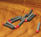 A collection of Hareline 1/16 inch High Viz Ant Bodies scattered on a wooden bench, showcasing the segmented grey foam cylinders accented with vibrant red indicator tags.