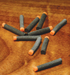 A collection of Hareline 1/16 inch High Viz Ant Bodies scattered on a wooden bench, showcasing the segmented grey foam cylinders accented with vibrant orange indicator tags.