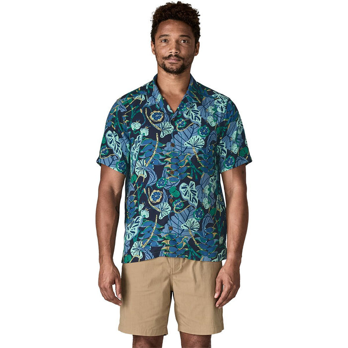 A man modeling a short-sleeve button-up camp shirt with a blue and green tropical leaf pattern, paired with khaki shorts, against a plain white background.