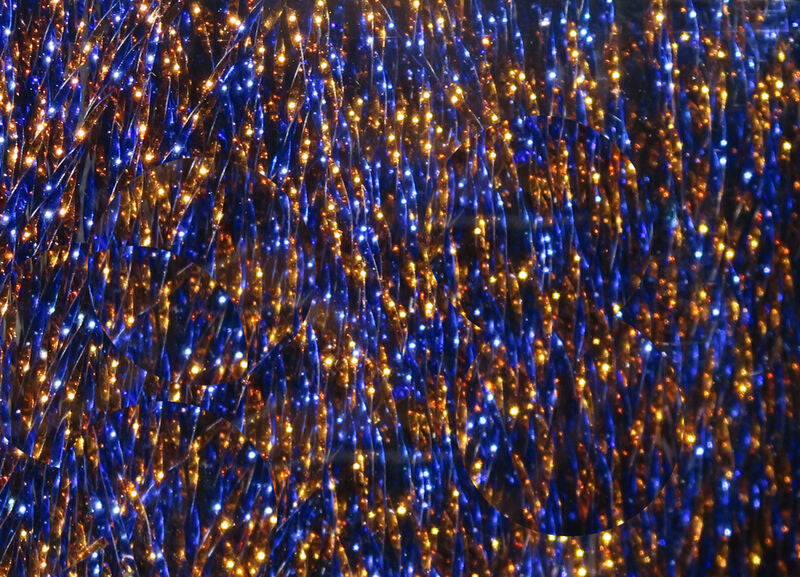 A close-up view of Hareline Grizzly Krystal Flash in Copper and Blue, showing a dense bundle of crinkled, highly reflective strands twisted with alternating metallic copper and deep blue segments.