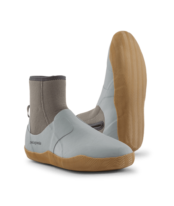 A pair of water shoes by Patagonia, featuring a white upper, a beige sock-like ankle collar, and a tan wavy-patterned sole, shown against a solid green background.