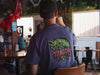 Angler wearing the grape Yakoda Drippy Trout fly fishing shirt while sitting at a fly tying bench outdoors.