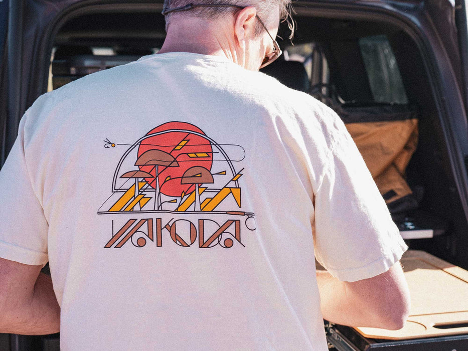Angler at a truck tailgate wearing the ivory heavyweight Yakoda Prairie fly fishing shirt showing the back artwork.